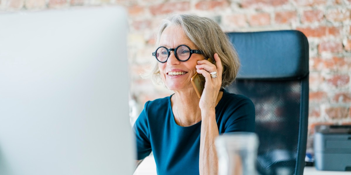 Uśmiechnięta kobieta rozmawia przez telefon przed komputerem