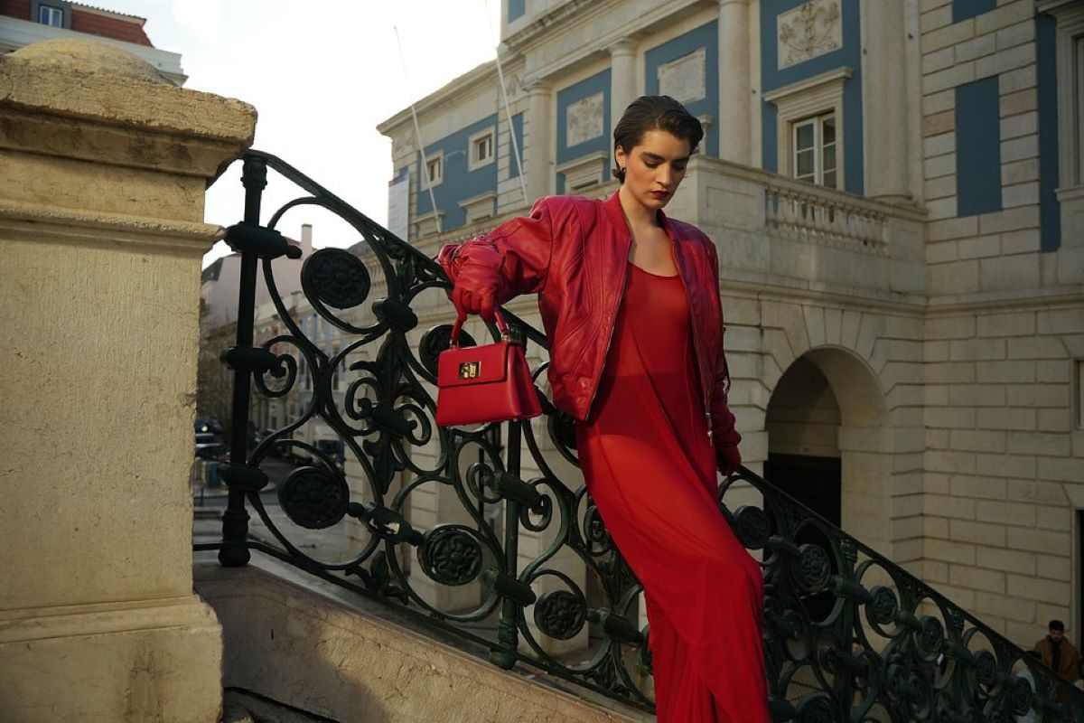 Notowana na warszawskim parkiecie spółka Answear opublikowała raport finansowy za III kwartał 2024 roku. I choć popularny e-commerce zmniejszył stratę względem zeszłego roku, to wypracowane przez niego dane były gorsze niż zakładali obserwatorzy rynku. Jak na wyniki Answear zareagowali inwestorzy oraz jakie są prognozy spółki wobec IV kwartału? Dokładnie przeanalizowaliśmy otrzymany raport. Zdjęcie z kampanii wypływającej na wyniki Answear. Modelka oparta o poręcz zabytkowych schodów. Kobieta ubrana w długą czerwoną sukienkę, na którą nałożyła czerwoną skórę. Jej stylizację uzupełniają czerwone rękawiczki oraz czerwona torebka trzymana w prawej dłoni.