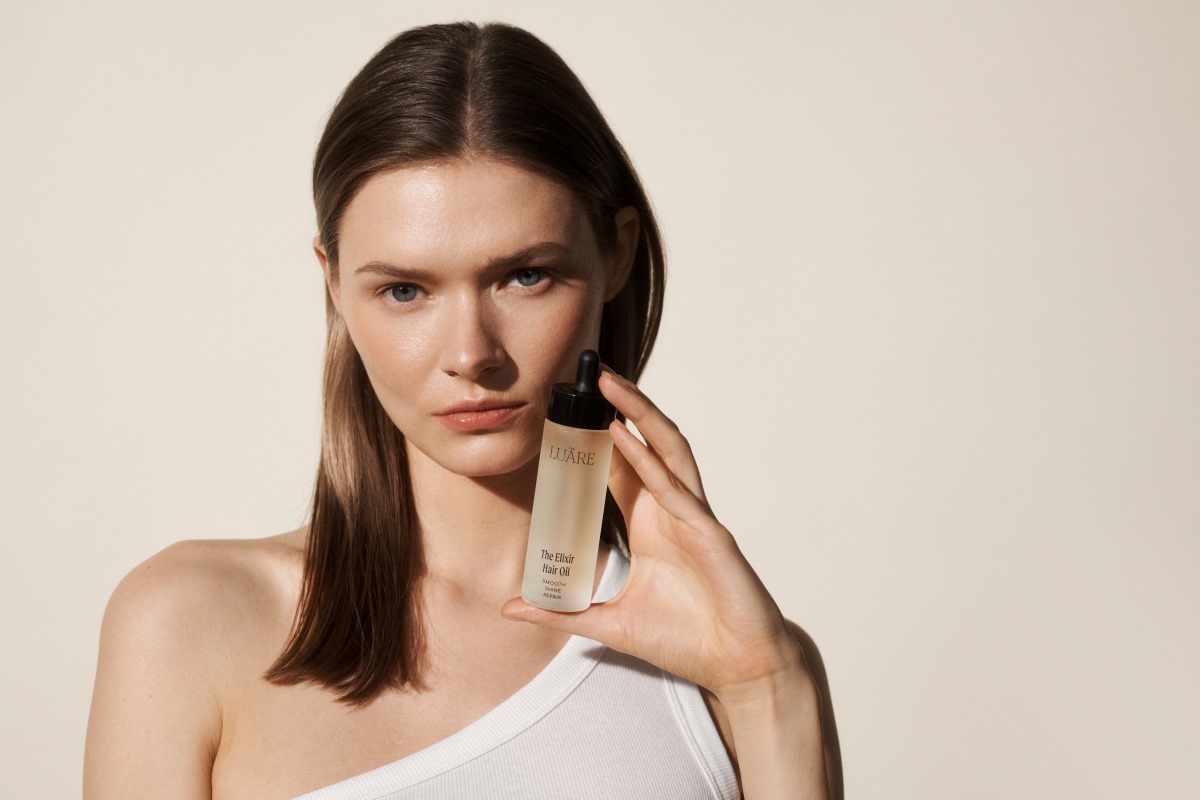 Przez lata współpracowała z największymi detalistami oraz z sukcesami rozwijała markę odzieżową. Teraz przyszedł czas na kolejny krok w jej karierze. Monika Frydrych debiutuje z Luare, pierwszą polską luksusową marką w segmencie hair care, która zrewolucjonizuje rynek czystymi składami produktów oraz ręcznie wytwarzanymi akcesoriami. Jakie wartości wpisane są w DNA Luare oraz co klienci znajdą w ofercie marki? Kadr portretowy na modelkę trzymającą w prawej dłoni produkt z linii kosmetyków Luare. Kobieta ma niebieskie oczy i długie brązowe włosy.