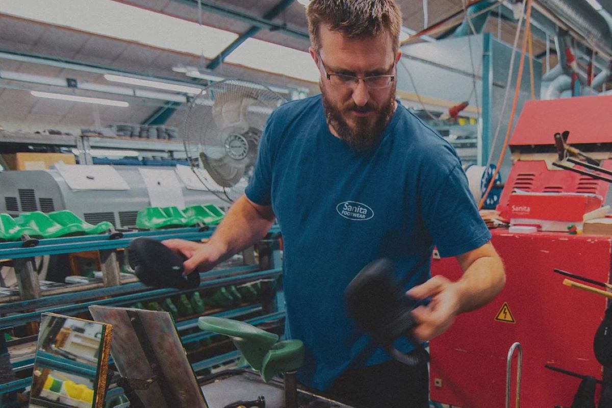 Nie takiego początku roku spodziewali się Polacy zatrudnieni w strukturach mieszczącego się w Pile zakładu produkcyjnego duńskiej marki Sanita. Choć zdawali sobie oni sprawę ze złego stanu finansów zatrudniającej ich fabryki, to dotychczas nie otrzymali wypowiedzeń. Ich pracodawca nie pokazał im również wniosku upadłościowego. Zdecydował się natomiast za pośrednictwem nieoficjalnych kanałów przekazać wiadomość: „Nie przychodźcie już do pracy”. Czy oznacza to bankructwo fabryki w Pile? Na zdjęciu widoczny jest mężczyzna z brodą, ubrany w niebieską koszulkę z logo "Sanita Footwear". Pracuje w zakładzie produkcyjnym, trzymając w rękach elementy obuwia. W tle widać taśmociąg z formami na buty w kolorze zielonym, przemysłowe maszyny oraz wentylator. Otoczenie wskazuje na proces produkcji obuwia w profesjonalnej fabryce, a logo "Sanita" podkreśla związek z marką specjalizującą się w produkcji komfortowych butów.