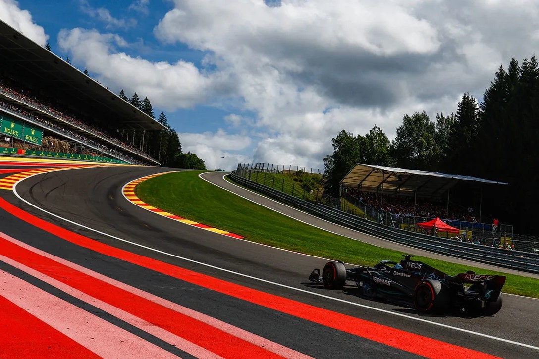 Adidas w Formule 1. Niemiecka marka odzieżowa i obuwnicza ogłosiła rozpoczęcie wieloletniej współpracy z Mercedesem-AMG PETRONAS, stając się oficjalnym dostawcą sprzętu dla całego zespołu. Opublikowana informacja oznacza rozstanie z dotychczasowymi partnerami technicznymi – Pumą i Tommy Hilfigerem. Czy Adidas z sukcesami zaprezentuje się w sezonie otwierającym erę bez Lewisa Hamiltona? Na zdjęciu widzimy bolid Mercedesa F1 na legendarnym torze Spa-Francorchamps, który dynamicznie pokonuje zakręt otoczony zielenią i trybunami pełnymi kibiców. Sceneria podkreśla emocje związane z wyścigami oraz współpracę "Adidas F1", która wnosi nową jakość i styl do świata Formuły 1.