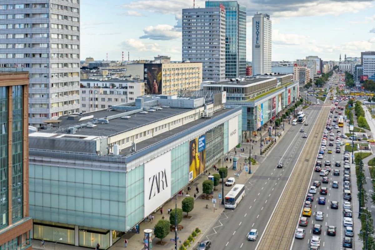 Zara, jeden z najbardziej rozpoznawalnych salonów hiszpańskiej sieci Inditex w centrum Warszawy, zniknęła z Domów Towarowych Wars Sawa Junior. Co ważne – nie pozostawi to jednak pustki w prestiżowej przestrzeni przy ul. Marszałkowskiej 104-122. Według nieoficjalnych informacji, wkroczy tam bowiem japoński gigant odzieżowy, Uniqlo, planujący dalszą ekspansję w Polsce. Widok z lotu ptaka na ulicę Marszałkowską w Warszawie, z dużym budynkiem handlowym, na którym znajduje się logo sklepu Zara na Marszałkowskiej. Po prawej stronie ulica z tramwajami i ruchem samochodowym, a w tle wysokie wieżowce, w tym hotel Novotel. Wzdłuż chodników poruszają się piesi.
