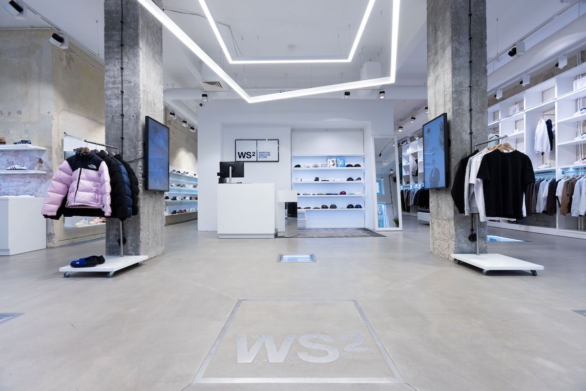 Nowoczesne wnętrze sklepu Warsaw Sneaker Store, z minimalistycznym designem, jasnym oświetleniem LED, półkami z butami i akcesoriami oraz ekspozycją odzieży. Warsaw Sneaker Store należy do Szopex, który właśnie przejął CCC.