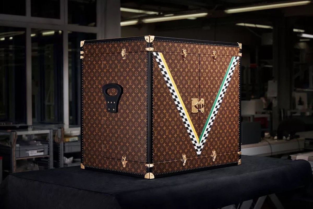 Luksusowy kuferek Louis Vuitton w klasycznym monogramowym wzorze, ozdobiony dużym motywem 'V' w barwach wyścigowych: zieleni, bieli i czerni w szachownicę. Solidne złote okucia i zamki podkreślają elegancję, a design nawiązuje do estetyki Formuły 1.