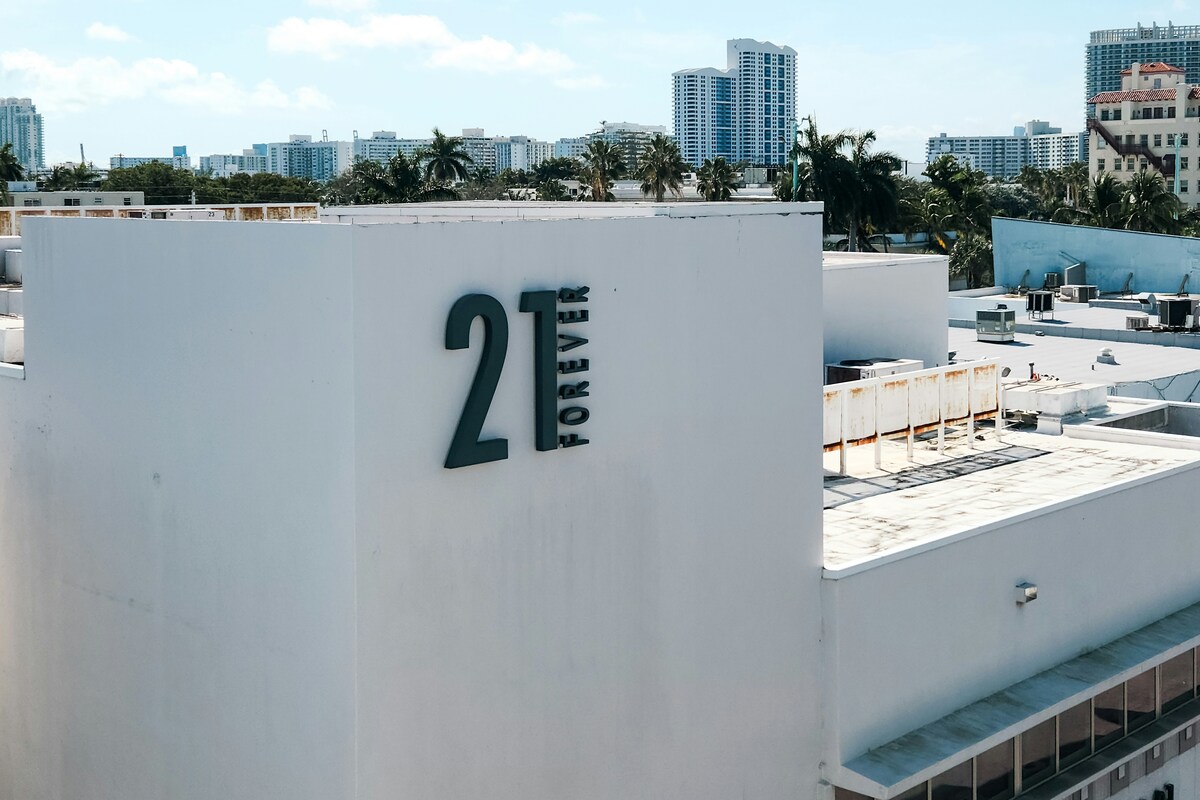 Forever 21. Na zdjęciu widać biały budynek sklepowy ze znakiem Forever 21. W tle widać panoramę miasta.