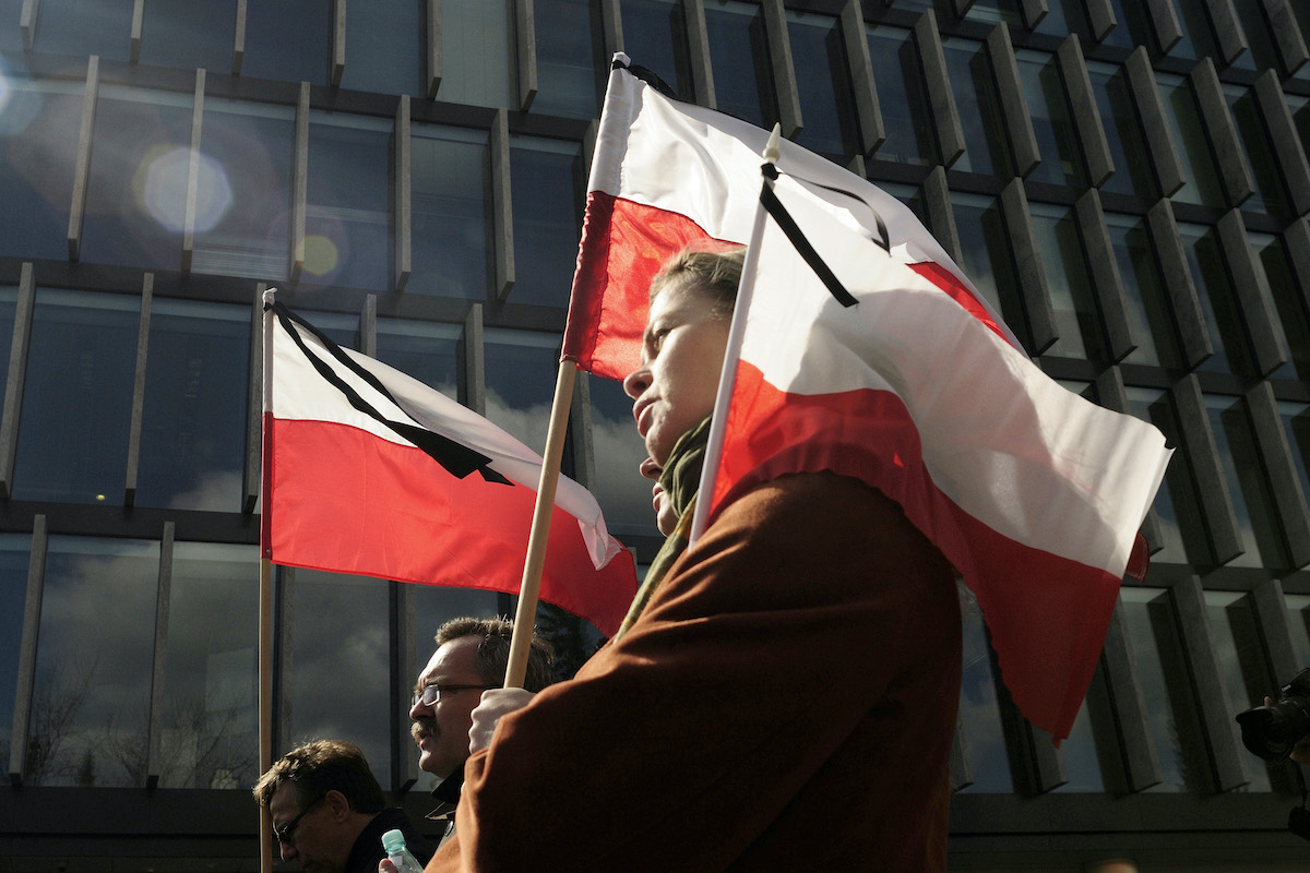Żałoba narodowa w Polsce 26 kwietnia 2025 r. Co to oznacza - czy sklepy będą otwarte? Na zdjęciu widać ludzi idących z polskimi flagami, oznaczonych czarnymi wstążkami jako znakiem żałoby narodowej.