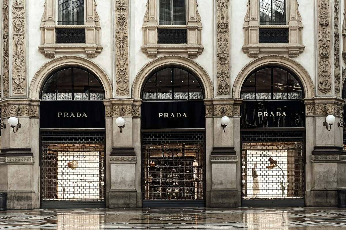 Wyniki finansowe Prady. Zewnętrzna część zabytkowego budynku, w którym mieści się butik Prady. Widoczne wejście, witryny sklepowe i szyldy marki.