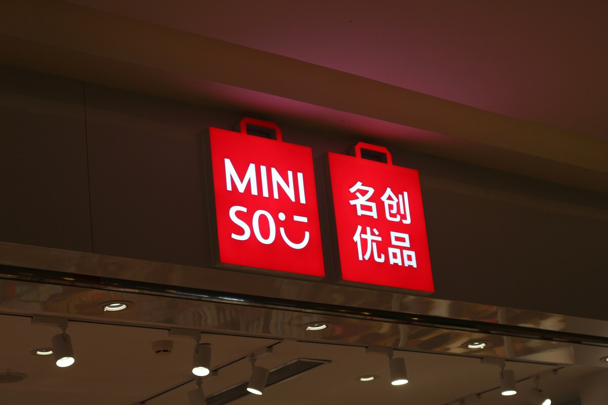 Sklep Miniso Polska. Zdjęcie szyldu z logo Miniso – czerwone torby zakupowe z białym napisem. Zawieszone nad wejściem do sklepu.