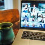 Laptop i filiżanka kawy obok. Na ekranie widoczny jest webinar.
