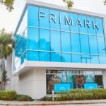 Aplikacja mobilna Primark. Zdjęcie sklepu stacjonarnego Primark z niebieską fasadą i białym szyldem. Budynek otoczony jest palmami.