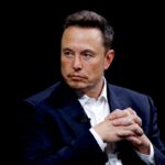 To zdjęcie przedstawia Elona Muska podczas oficjalnej inauguracji Donalda Trumpa. Musk, ubrany w elegancki, ciemny garnitur, siedzi z założonymi rękami, co nadaje mu spokojny, ale skupiony wyraz twarzy. Jego poważna mina podkreśla wagę i wagę wydarzenia, w którym bierze udział. To kultowe zdjęcie ukazuje moment, w którym biznes i polityka spotykają się na najwyższym szczeblu, podkreślając rolę Muska jako jednego z najbardziej wpływowych wizjonerów technologicznych współczesności.