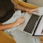 Polska ustawa o dostępności będzie nakładać surowe kary na e-biznesy, które nie spełnią tych wymogów. Na zdjęciu kobieta siedzi na żółtej kanapie z laptopem na kolanach i przegląda ofertę internetowego sklepu odzieżowego.