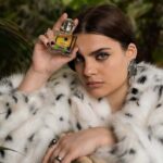 Modelka nosi perfumy Avon – firmy kosmetycznej rozwijającej model franczyzowy w Polsce. Kobieta ma ciemne włosy związane z tyłu i nosi białe futro w czarne kropki.