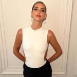 Influencerzy sektora luksusowego w 2025 roku. Zdjęcie: Chiara Ferragni, wiodąca influencerka w branży luksusowej. Ubrana w uniesione włosy, biały top bez rękawów i czarną spódnicę, pozuje na tle białej, teksturowanej ściany.