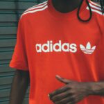 Zbliżenie na raport finansowy firmy Adidas za drugi kwartał 2025 r., na którym widać mężczyznę ubranego w czerwoną koszulkę z logo marki.