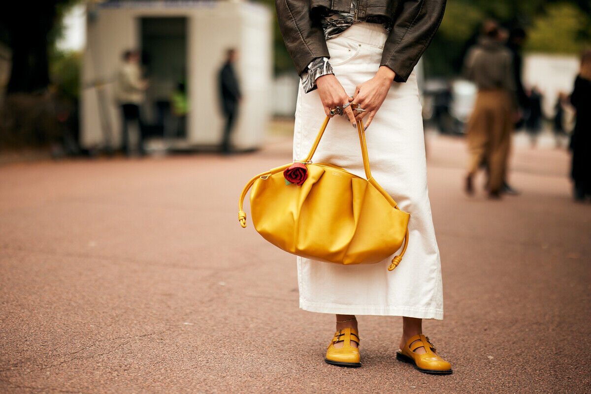 Odsyłki produktów stały się normalną częścią dzisiejszego handlu, lecz ich koszt zaczyna osiągać rozmiary, których nie można lekceważyć. Według nowego sprawozdania National Retail Federation (NRF), w 2025 roku wartość zwróconych artykułów osiągnie 849,9 mld dolarów – to aż 15,8% ogólnej sprzedaży detalicznej. Dla segmentu retail to nie tylko trudność w obszarze logistyki. To znak, że model sprzedaży bazujący na nagłych zakupach, bezpłatnych zwrotach i ekspresowej dostawie zaczyna się finansowo i ekologicznie nie spinać. Raport zwrotów. Fotografia przedstawia osobę stojącą na ulicy, z uwzględnieniem jej kreacji i dodatków od pasa w dół. Osoba ta dzierży obszerną, pomarszczoną, żółtą torbę, zdobioną czerwoną różą. Ma na sobie długą spódnicę w odcieniu złamanej bieli lub beżu oraz brązową marynarkę albo bluzkę widoczną w górnej partii ujęcia. Na przegubach rąk widoczne są fragmenty koszuli lub bluzki oraz sygnety na palcach. Na stopach widnieją żółte trzewiki w stylu Mary Jane lub mokasyny z klamrą.