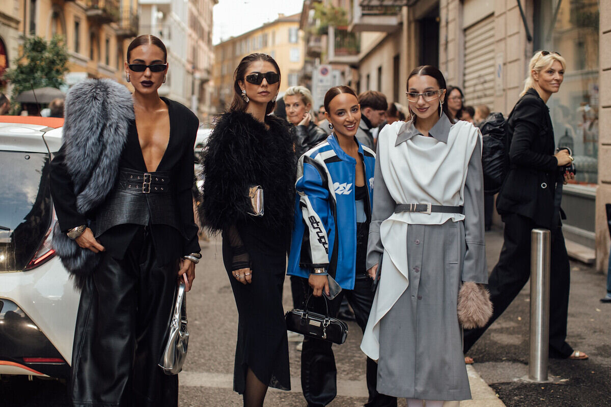 Petycja BFMA „Moja twarz należy do mnie”. Fotografia uśmiechniętych modelek. Cztery kobiety pozujące na ulicy: dwie w czarnych stylizacjach total look, jedna w kurtce motocyklowej, a ostatnia w szaro-białym outficie.
