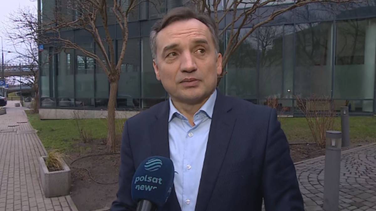 Mecenas Bartosz Lewandowski udzielający wywiadu dla Polsat News na tle nowoczesnego budynku.