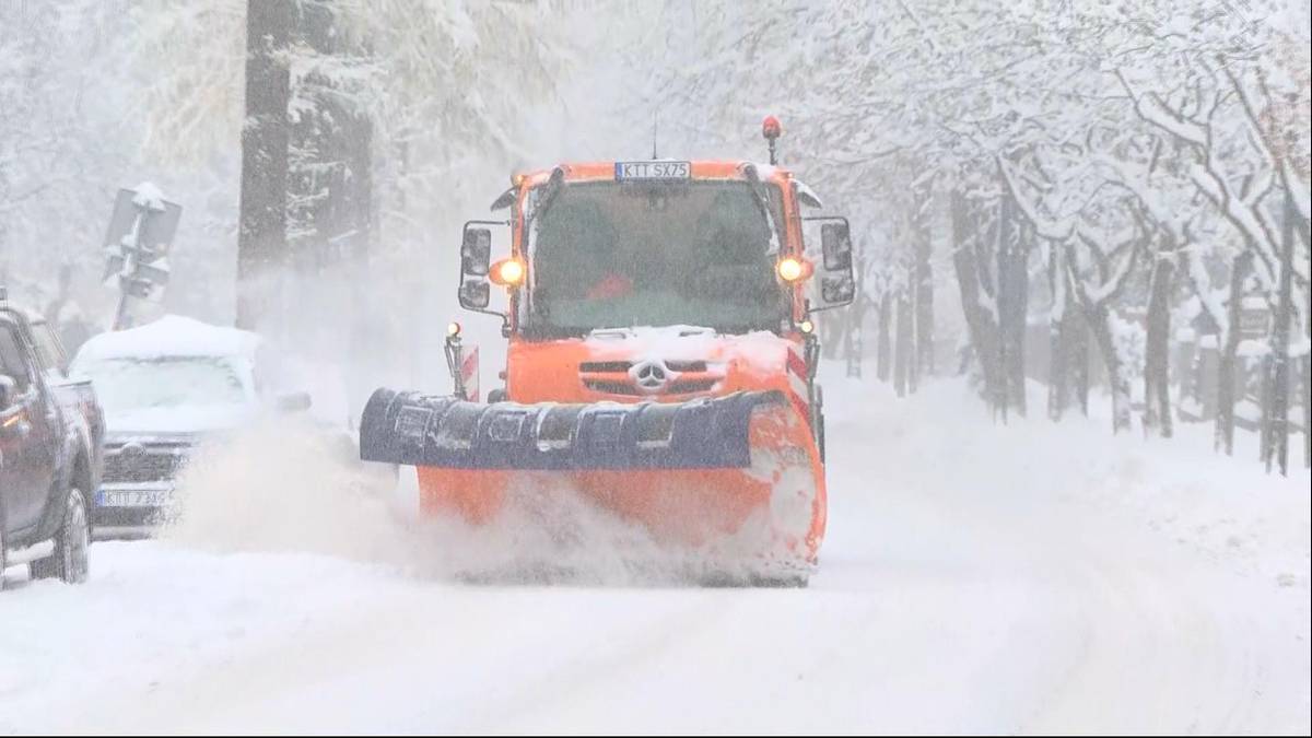 Pomarańczowy pług śnieżny z łyżką odśnieżającą na zaśnieżonej drodze podczas opad&oacute;w śniegu.