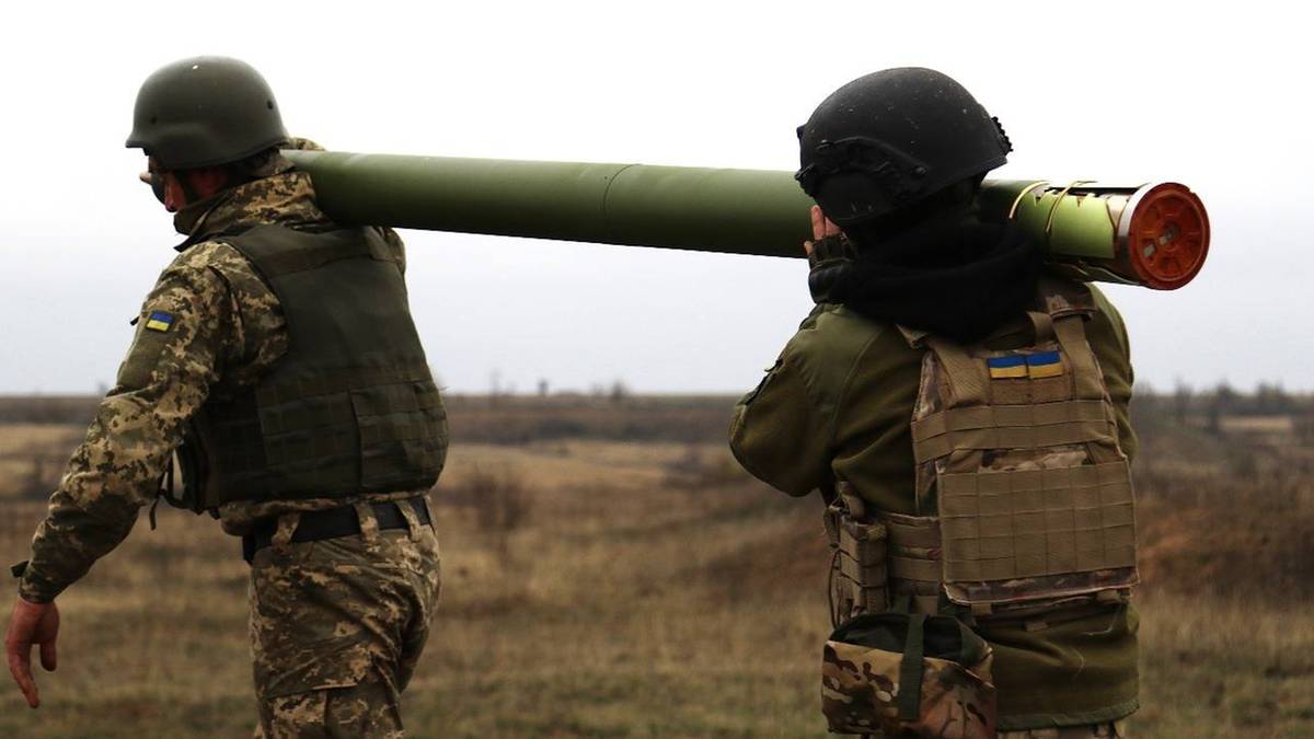Dw&oacute;ch żołnierzy w mundurach taktycznych i hełmach niesie na ramieniu długi, zielony pocisk.