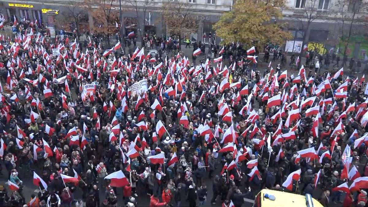 Tłum ludzi trzymających polskie flagi podczas zgromadzenia narodowego lub patriotycznego wydarzenia.