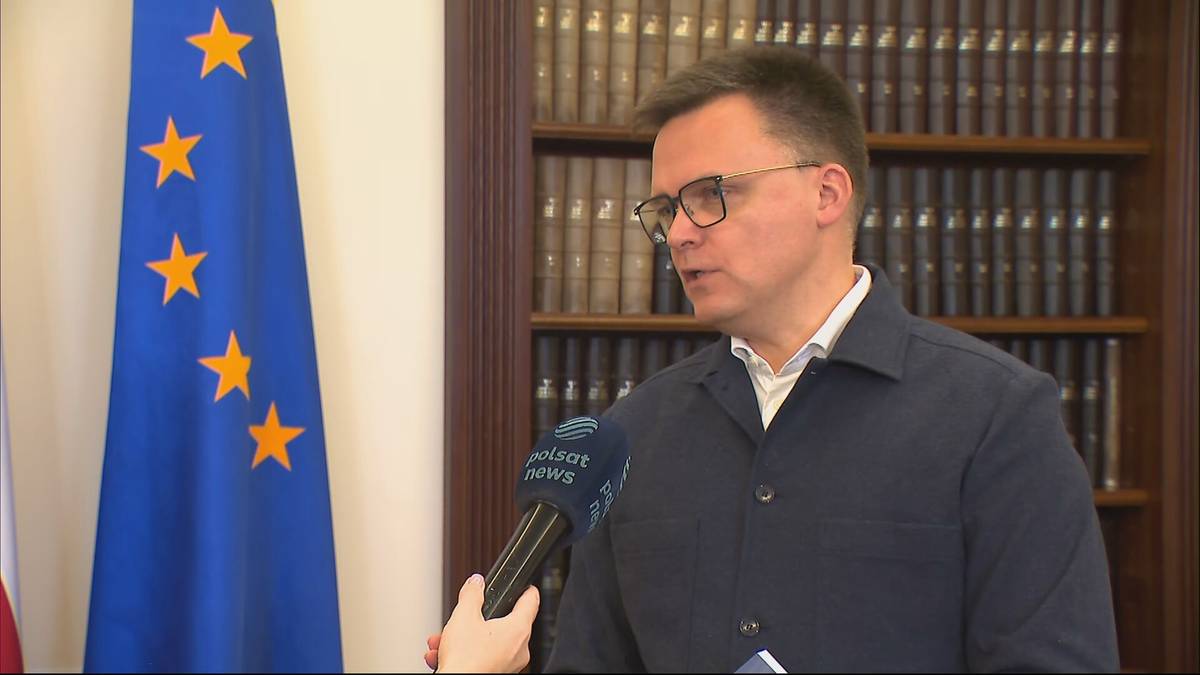 Szymon Hołownia udziela wywiadu reporterce Polsat News na tle flagi Unii Europejskiej.