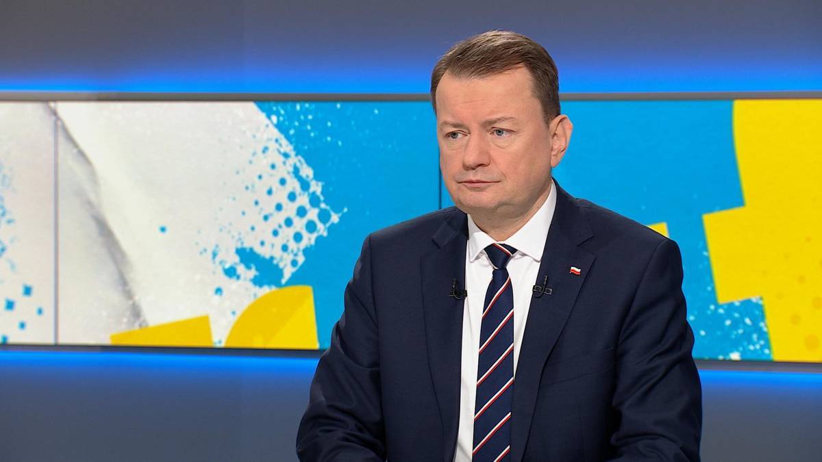 Mariusz Błaszczak pojawi się jako gość u Marcina Fijołka w audycji "Graffiti". Emisja od godziny 7:40 w stacjach Polsat, Polsat News oraz na witrynach Interii i polsatnews.pl. Mężczyzna w ciemnym garniturze i pasiastym krawacie siedzi na tle ekranu z niebiesko-żółtymi wzorami graficznymi.