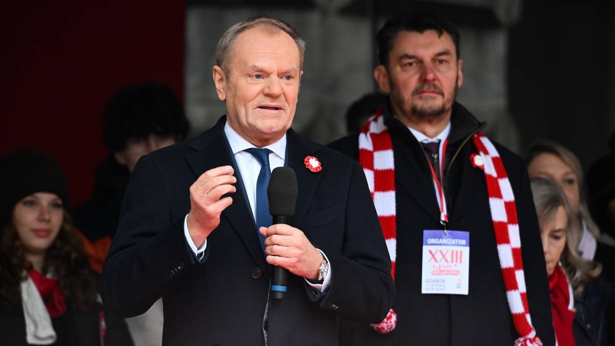 Premier Donald Tusk przemawia na tle grupy os&oacute;b, trzymając mikrofon.