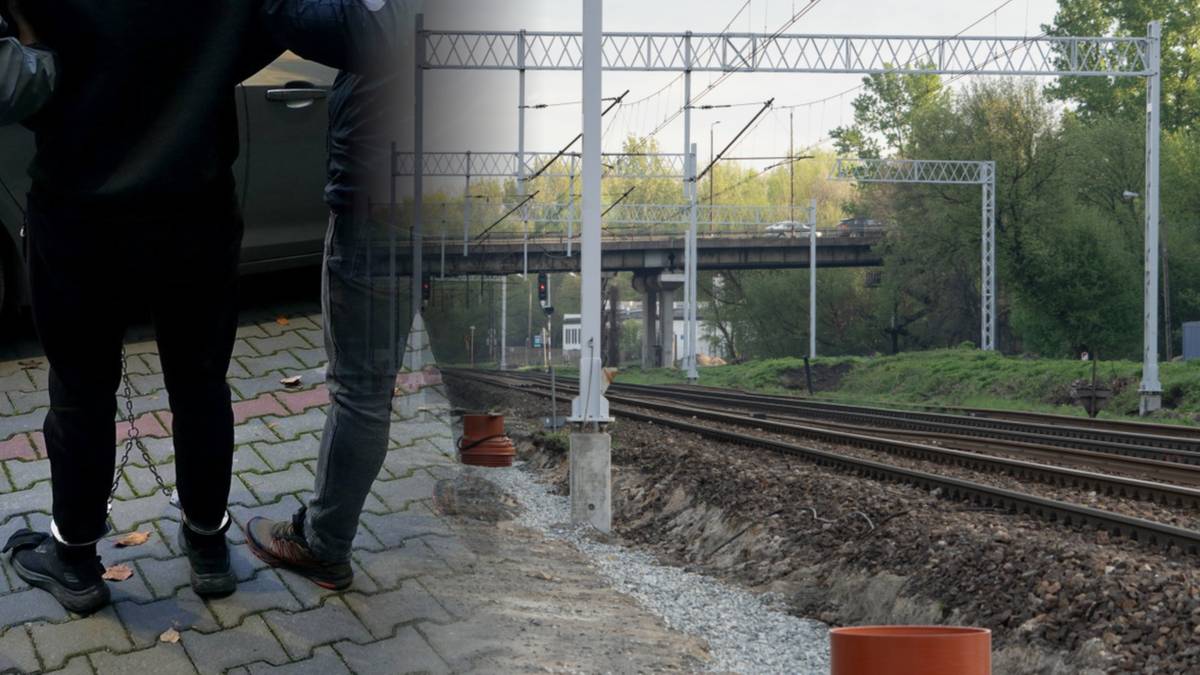 Fragment sylwetek dw&oacute;ch os&oacute;b stojących na chodniku obok torowiska kolejowego.