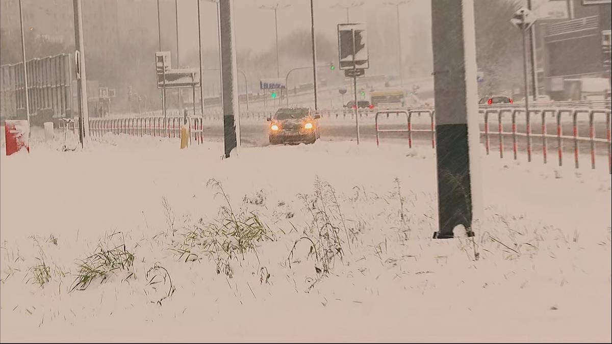 Droga pokryta grubą warstwą śniegu, po kt&oacute;rej porusza się ż&oacute;łty samoch&oacute;d podczas opad&oacute;w śniegu.