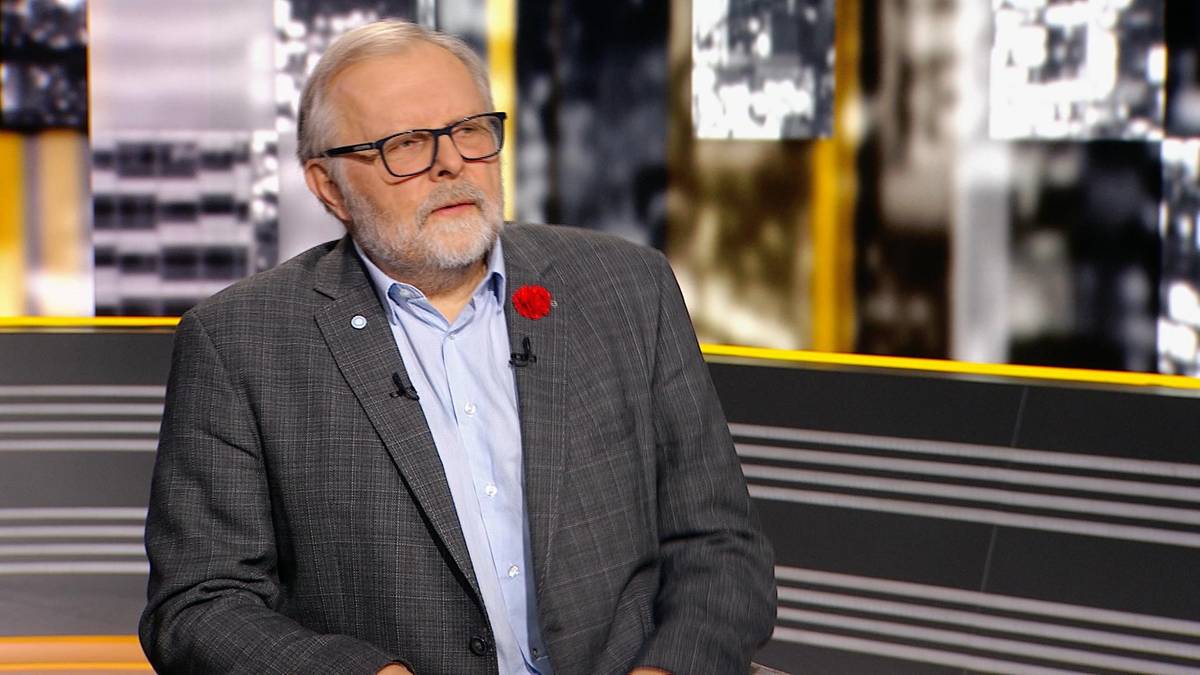 Profesor Szymon Malinowski w okularach i marynarce siedzi w studiu telewizyjnym.