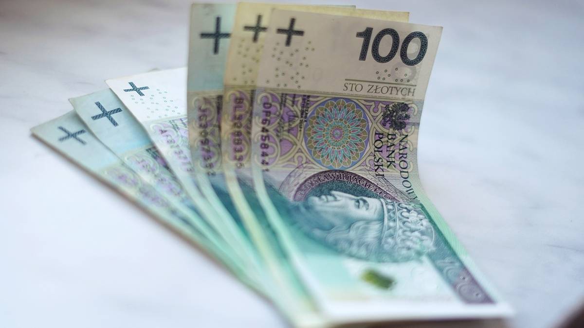 Kilka polskich banknot&oacute;w o nominale 100 złotych ułożonych wachlarzowo na jasnym tle.