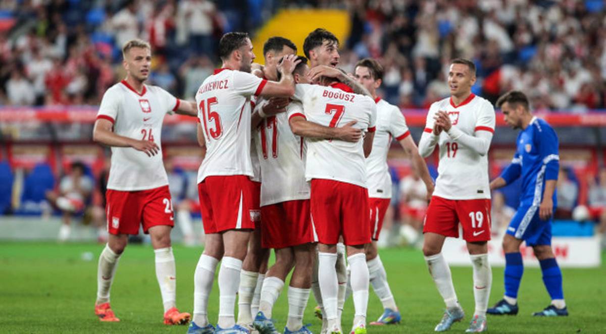 Trener Jan Urban ujawnił w piątek nazwiska graczy wyselekcjonowanych na listopadowe zgrupowanie kadry narodowej. W składzie znalazło się dwóch debiutantów. W ramach kwalifikacji do mistrzostw świata biało-czerwoni zmierzą się z Holandią oraz Maltą. Piłkarze reprezentacji Polski w białych strojach z czerwonymi akcentami cieszą się na boisku, kilku zawodników przytulonych świętuje sukces.