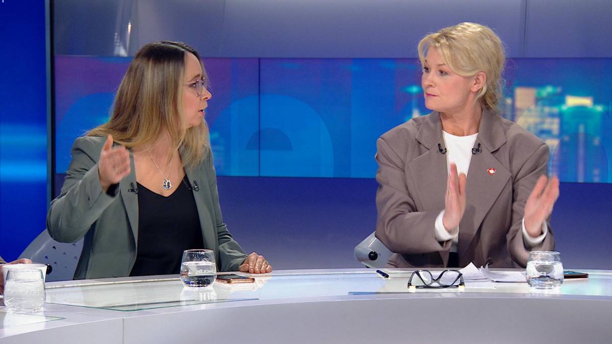 Dwie kobiety siedzą przy stole podczas dyskusji w studiu telewizyjnym. Kobieta po lewej gestykuluje prawą ręką, a kobieta po prawej ma złożone dłonie.