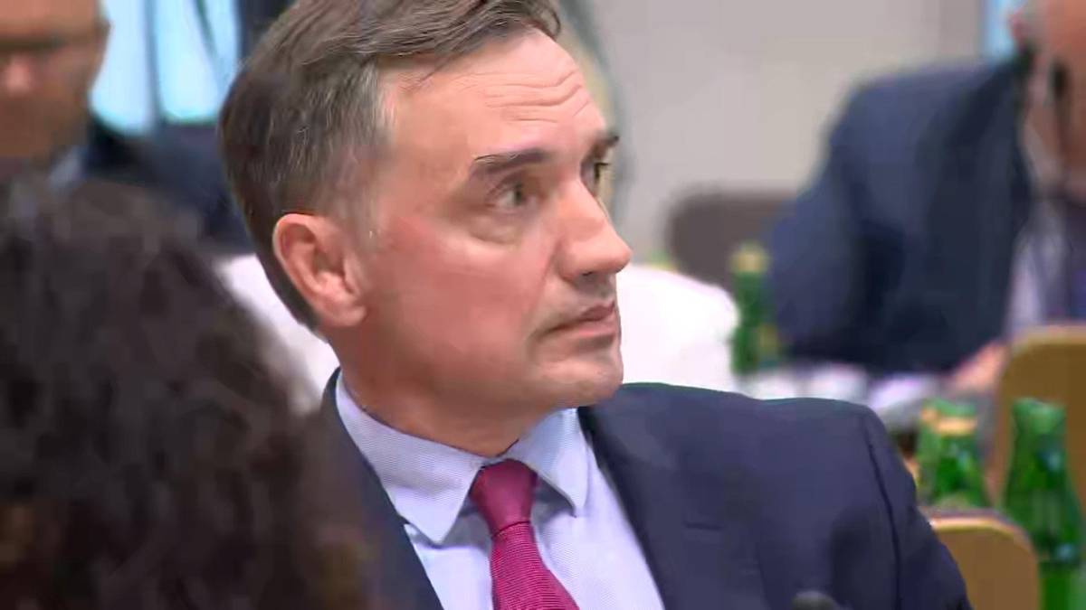 Mężczyzna w garniturze siedzi przy stole, słucha.