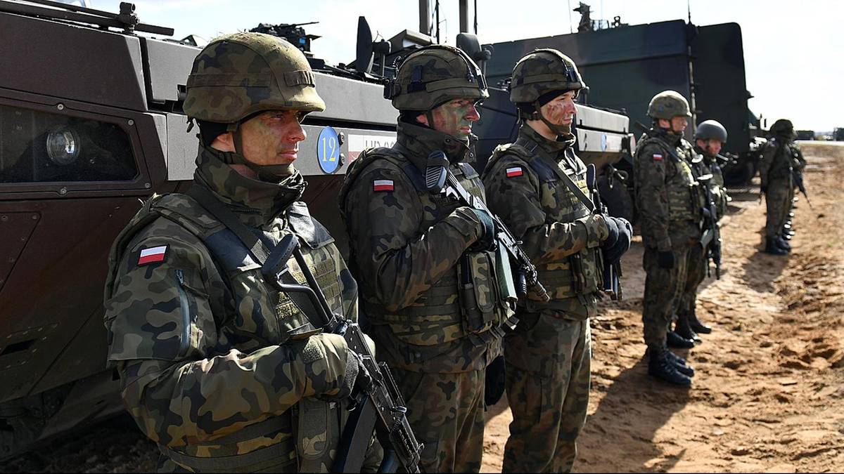 Żołnierze w mundurach polowych i hełmach stoją w szeregu obok pojazdu wojskowego.