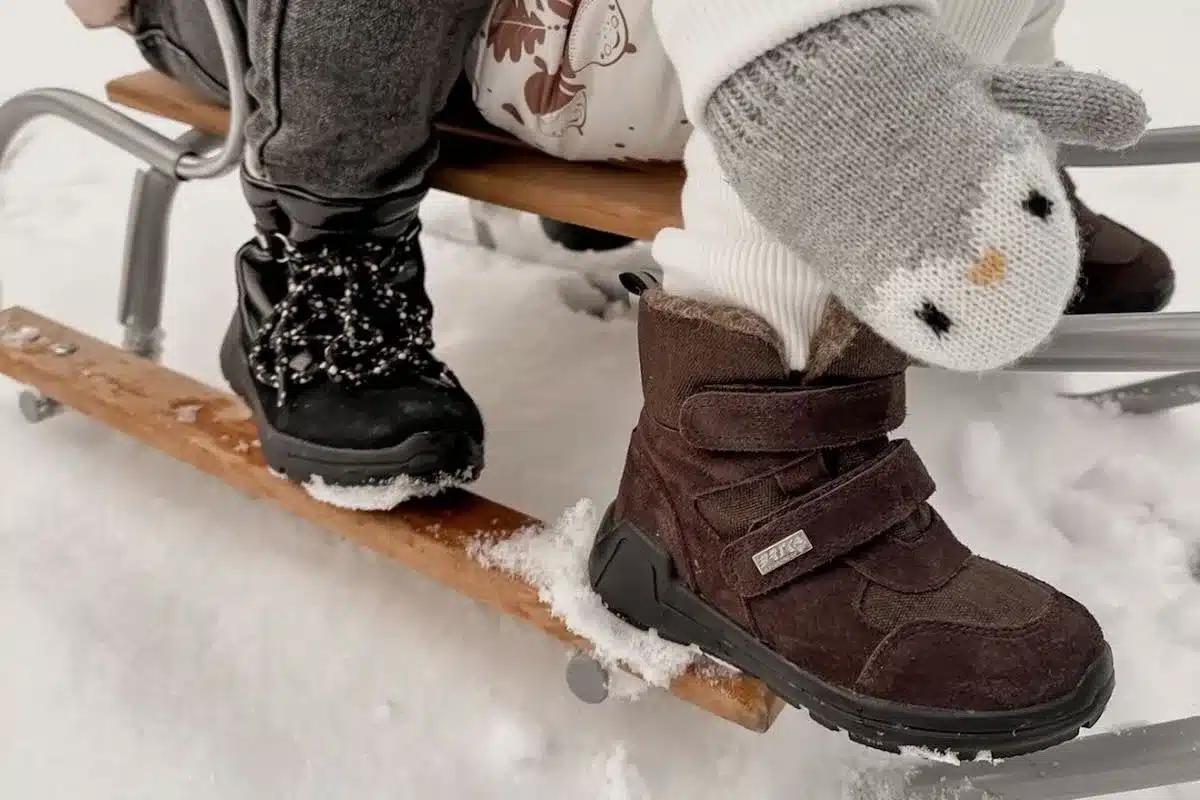 Polski producent obuwia Bartek SA upada. Co dalej? Na zdjęciu zbliżenie na obuwie dziecięce - dzieci jadą na sankach po śniegu.