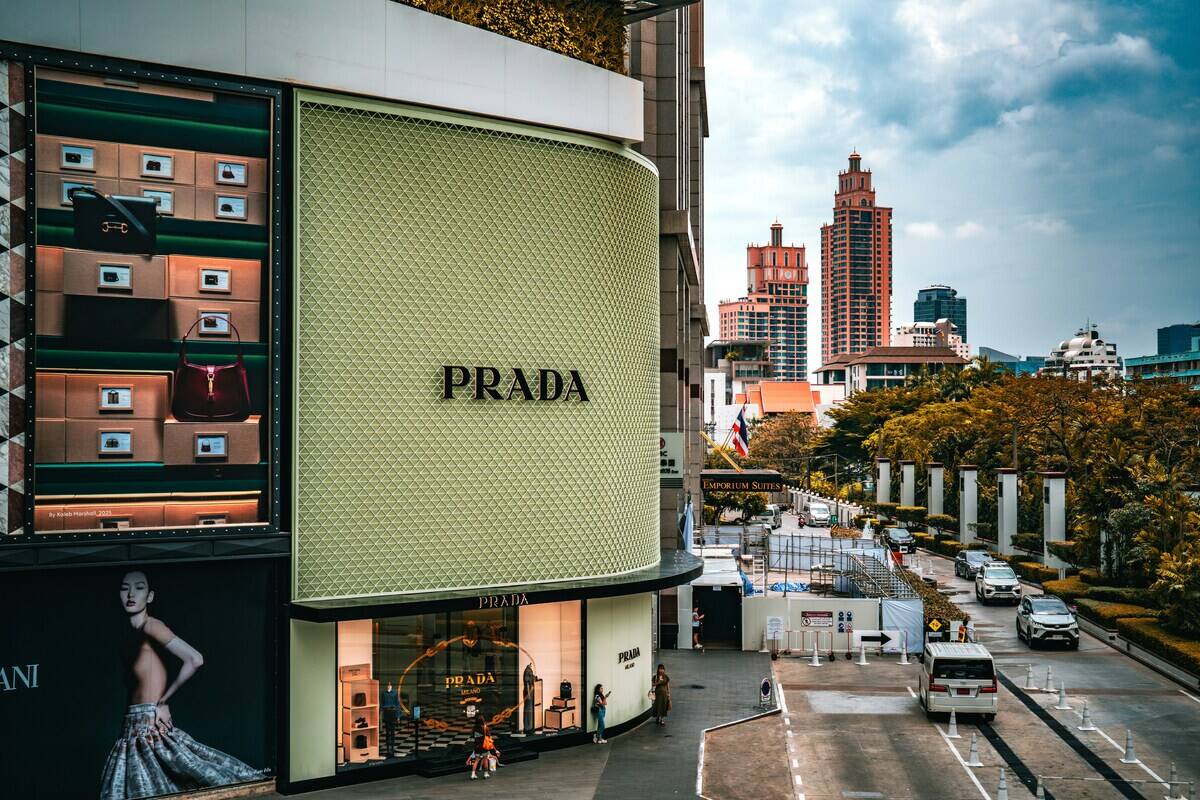Prada dostawcy koniec współpracy. Nowoczesny salon Prada w narożnym budynku w centrum miasta, z elegancką witryną i logo marki na tle ruchliwej ulicy oraz wysokich miejskich wieżowców.