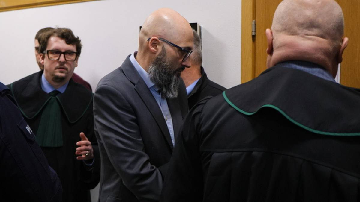 Trzech mężczyzn w togach prawniczych, dw&oacute;ch zwr&oacute;conych tyłem, jeden z brodą i okularami stojący profilem.