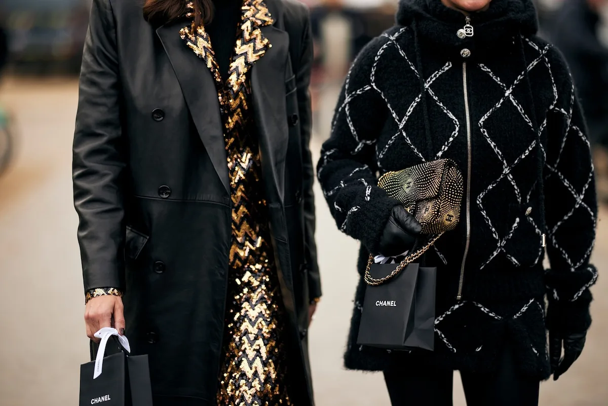 7 stycznia 2026 czy sklepy są otwarte? Na zdjęciu zbliżenie na sylwetki dwóch kobiet, odzianych na ciemno, jedna z nich dzierży torbę papierową Chanel.
