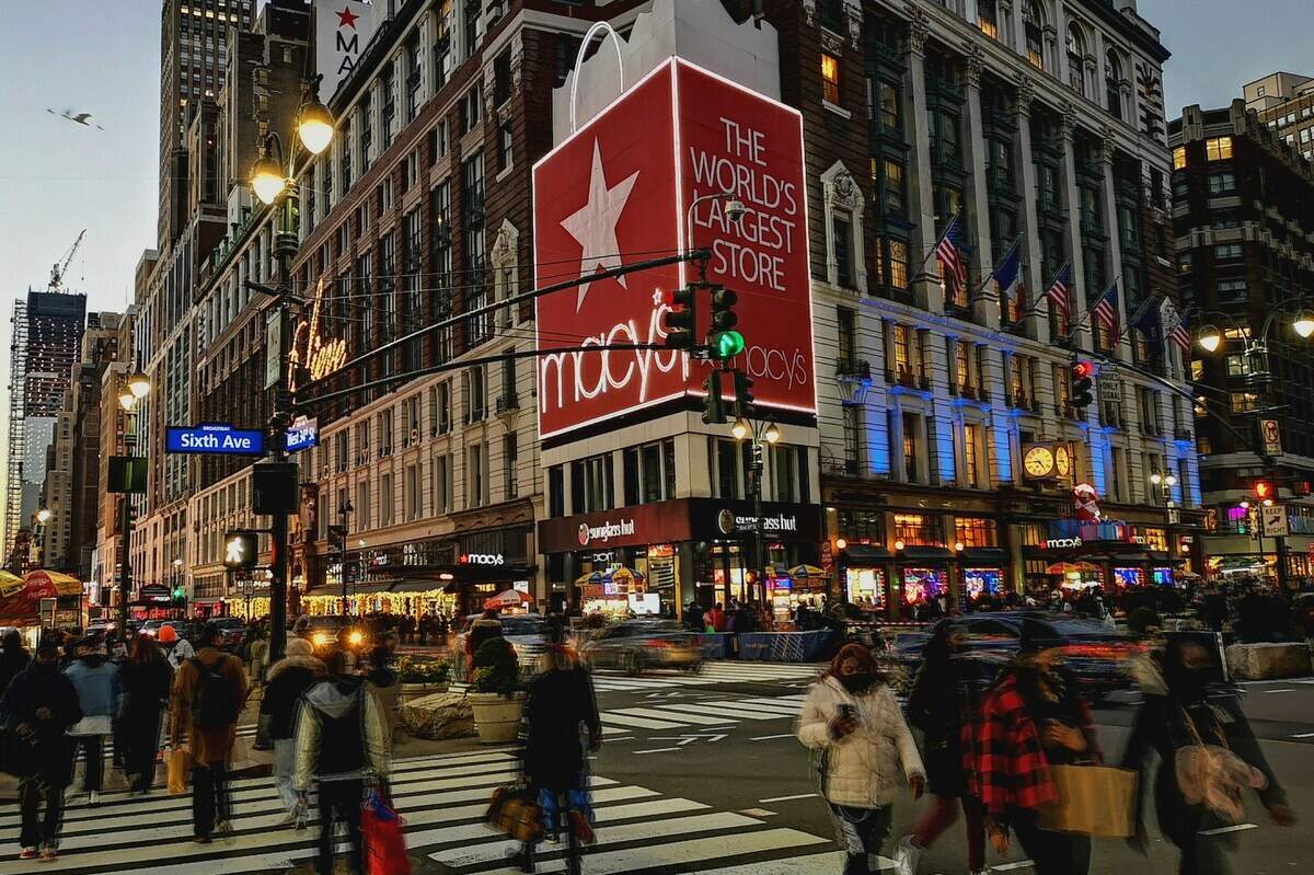Macy’s zwolnienia 2026. Ruchliwy wieczorny widok skrzyżowania na Herald Square w Nowym Jorku z charakterystycznym budynkiem Macy’s, podświetlonym czerwonym szyldem, przechodniami na pasach i intensywnym ruchem ulicznym w centrum miasta.