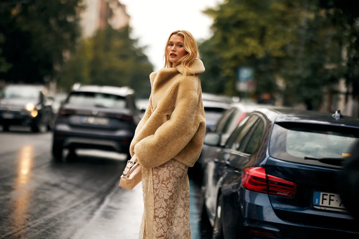 Podatek cyfrowy w Polsce. Kobieta w jasnym futrzanym płaszczu i koronkowej spódnicy stoi na miejskiej ulicy w deszczowy dzień, styl street style fashion.