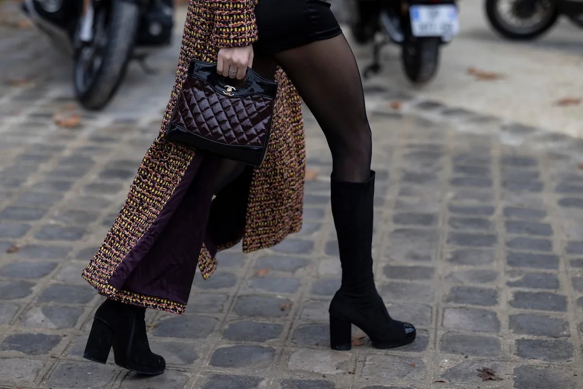 6 stycznia 2026 czy sklepy są otwarte? Na zdjęciu zbliżenie na idącą kobietę w wysokich czarnych butach i brązowym płaszczu, trzymającą w ręce torebkę chanel.