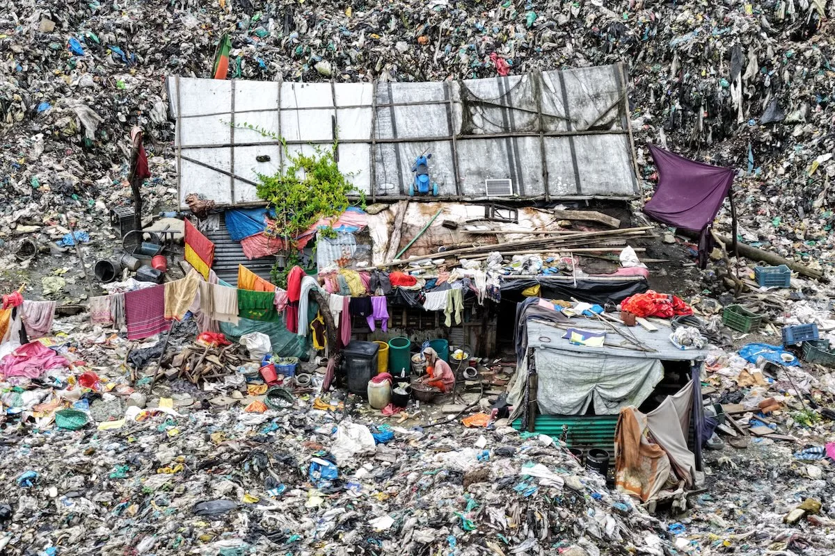 Nielegalne składowisko odpadów tekstylnych – góry zużytej odzieży i plastiku wokół prowizorycznych konstrukcji, ukazujące skalę problemu śmieci w sektorze mody.