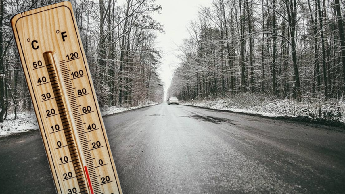 Drewniany termometr pokazujący ujemną temperaturę na tle zimowej, zaśnieżonej drogi