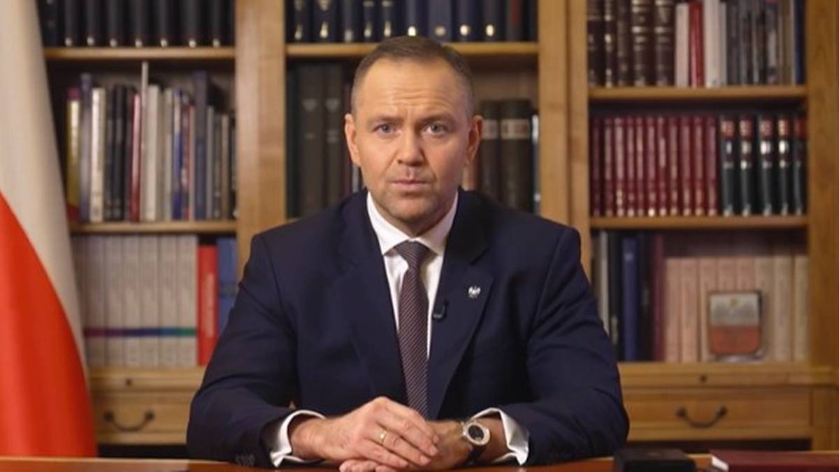 Prezydent Karol Nawrocki siedzi za biurkiem na tle biblioteczki.