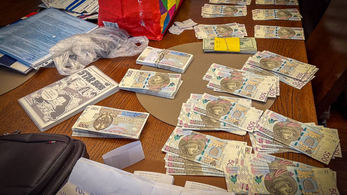 Rozłożone na stole banknoty o nominale 500 zł, dokumenty, torba i inne przedmioty.