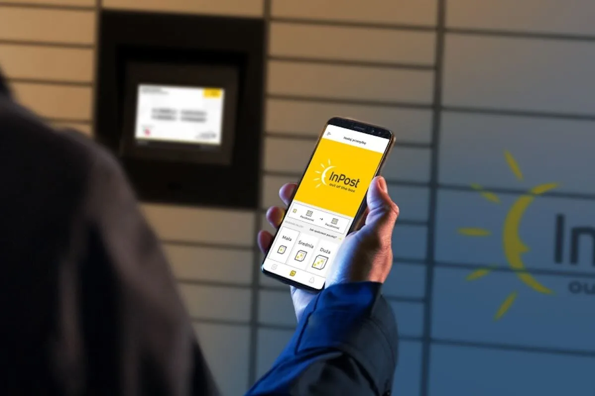 Zbliżenie na osobę trzymającą w ręce telefon z dużym żółtym logo InPost, stojącą na wprost paczkomatu