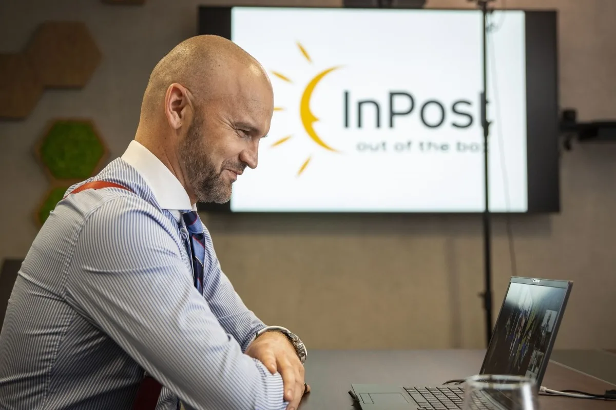 Czy InPost pozostanie polski po sprzedaży. Na zdjęciu Rafał Brzoska, CEO InPost siedzi wpatrzony w laptopa. W tle prezentacja z dużym logo InPost.