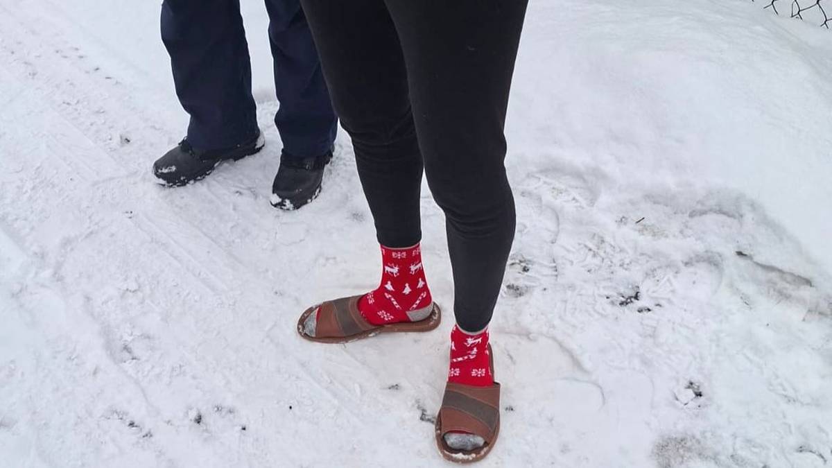 Nogi osoby w skarpetkach i klapkach na śniegu.